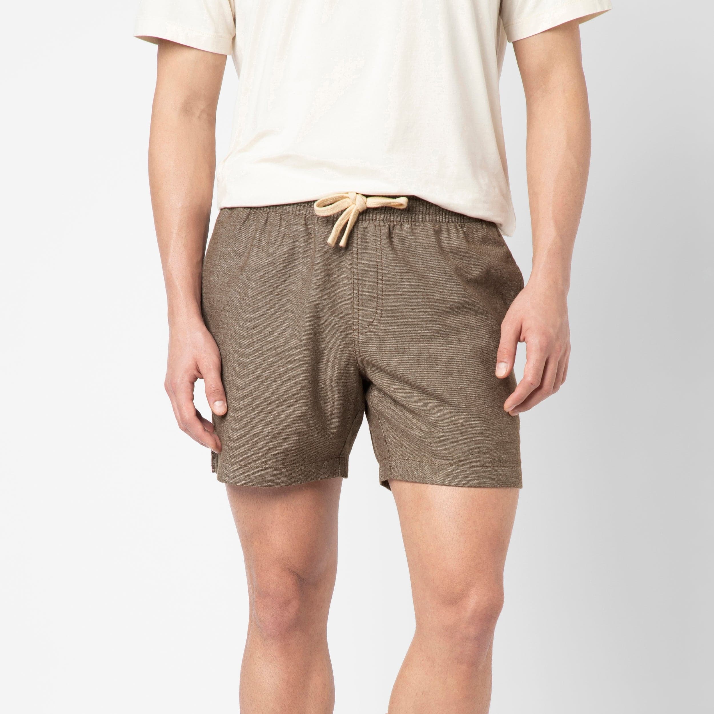 A person wearing a cream t-shirt and Bark Stretch Linen Short made from premium European linen stands against a plain white background with arms relaxed at their sides.